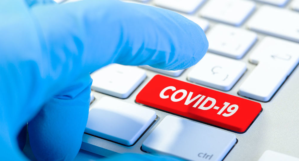 Hand with protecting glove and Keyboard with red key and COVID-19 message. Coronavirus concept